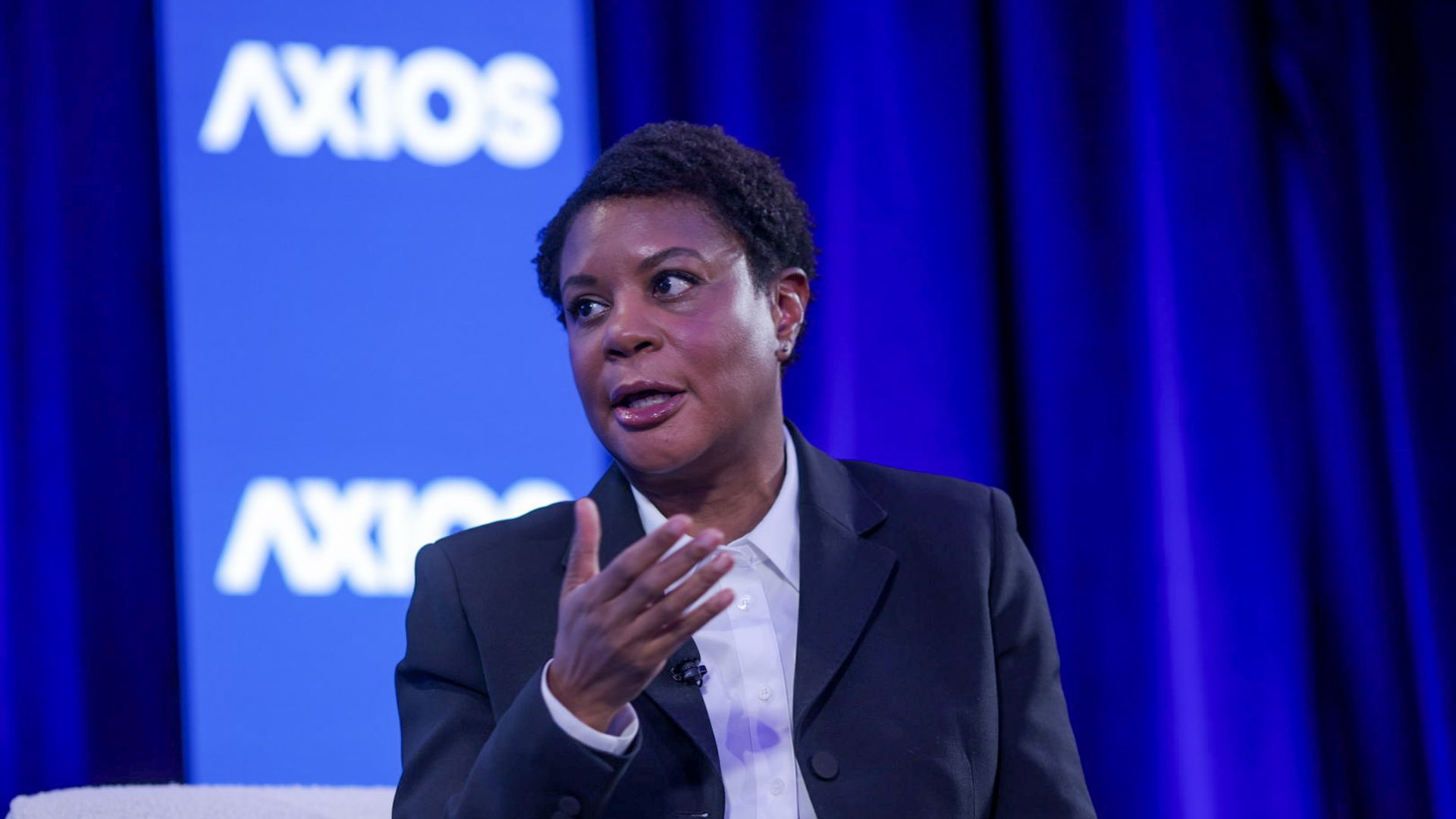 Alondra Nelson speaks with a hand outstretched, wearing a white shirt and dark jacket speaks in front of a blue background with AXIOS written in white